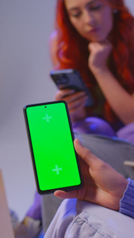 Close-Up-Vertical-Video-Studio-Shot-Of-Young-Gen-Z-Friends-Sitting-On-Sofa-Sharing-Social-Media-Post-On-Green-Screen-Mobile-Phone